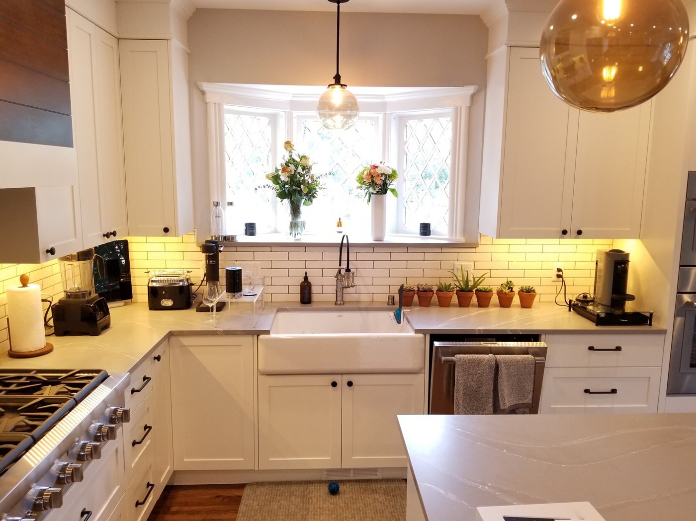Custom white kitchen cabinetry around a bay window with a farmhouse sink